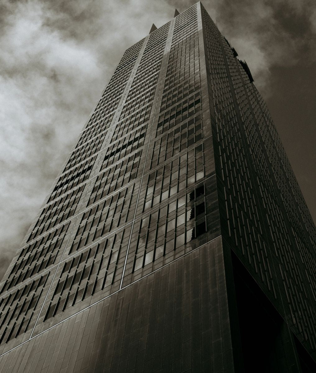 Dramatic black and white (monochrome) fine art photography print of a tall skyscraper, looking up toward the sky, titled Dystopian Dreams.